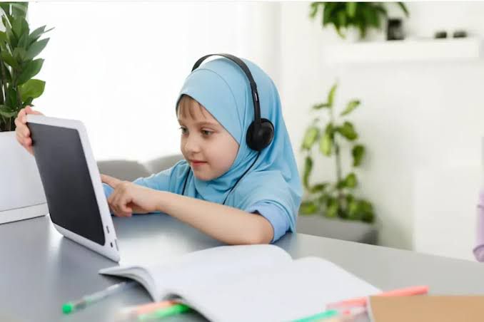 Young girl in hijab studying Quran on tablet